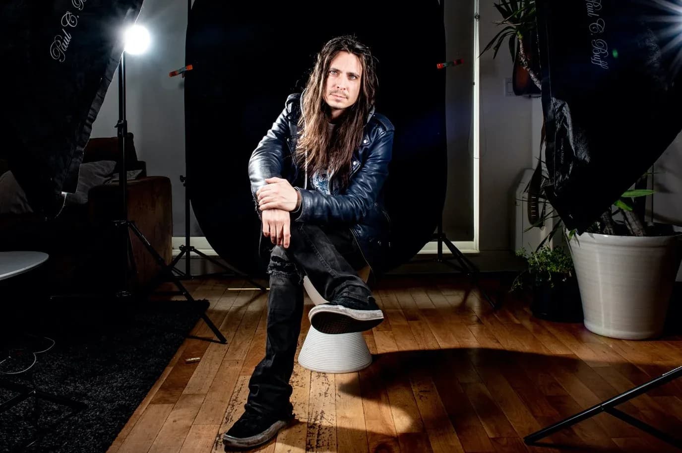Jonathan McPhail seated in a Greenpoint photography studio, lighting stands and a backdrop behind him.