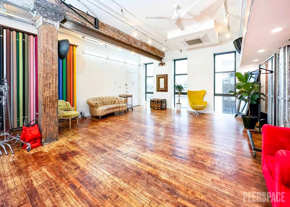 Spacious loft photography studio with colored paper backdrops, seating, and hardwood floor.