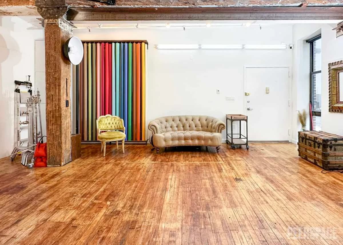 A photography studio with a row of colorful seamless backdrops, a tufted sofa, gold accent chair and lighting stands on a wood floor.