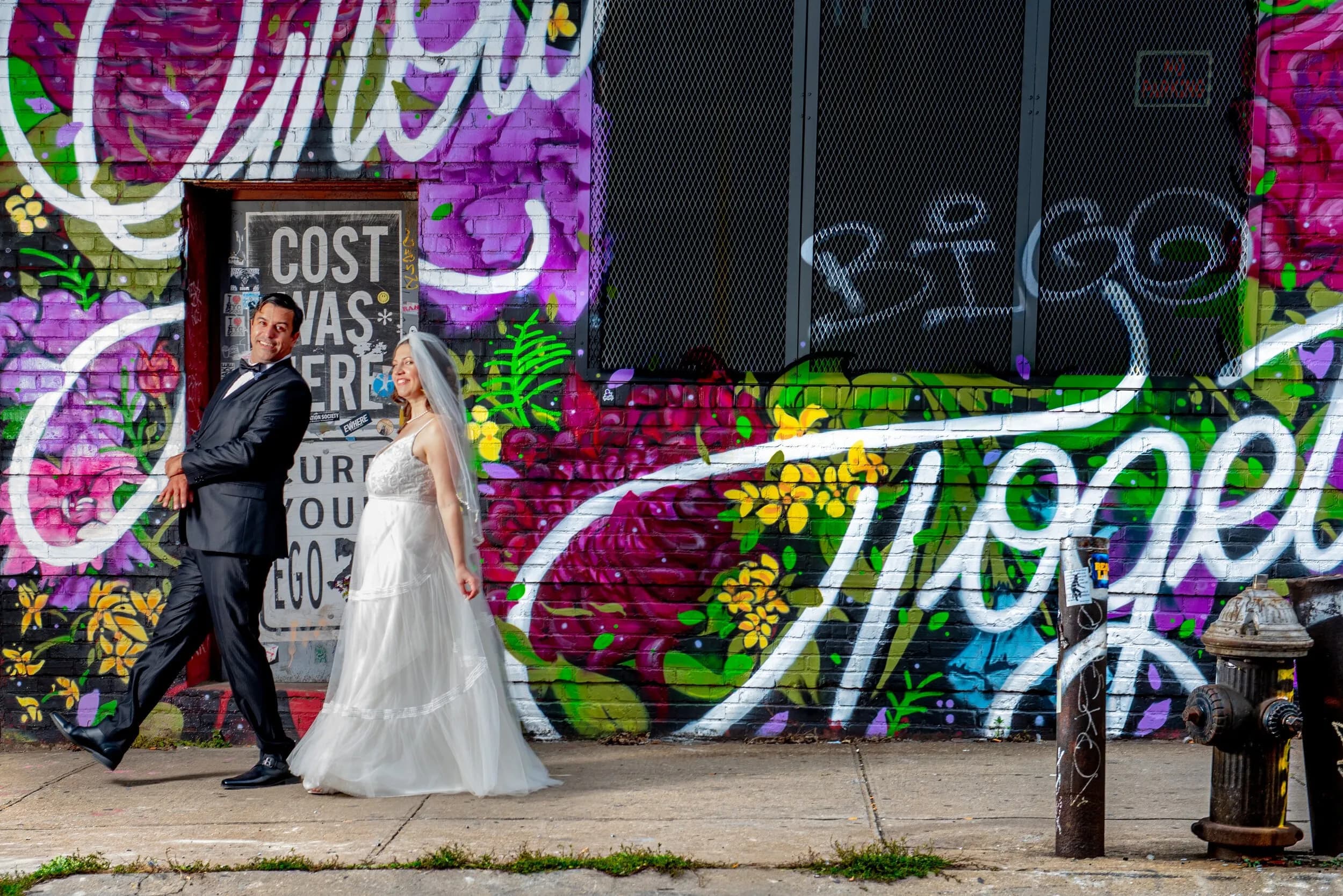 Bride and groom posing in front of a vibrant graffiti-covered wall on a city sidewalk